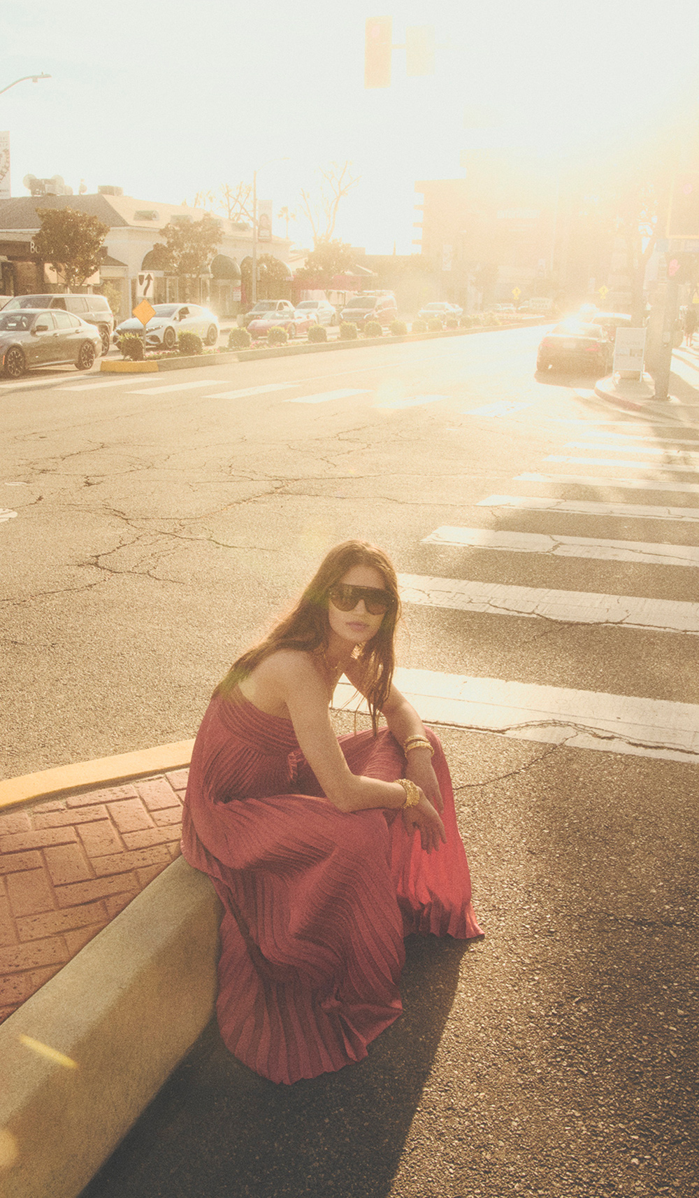 A model sitting on the street in a long pink dress