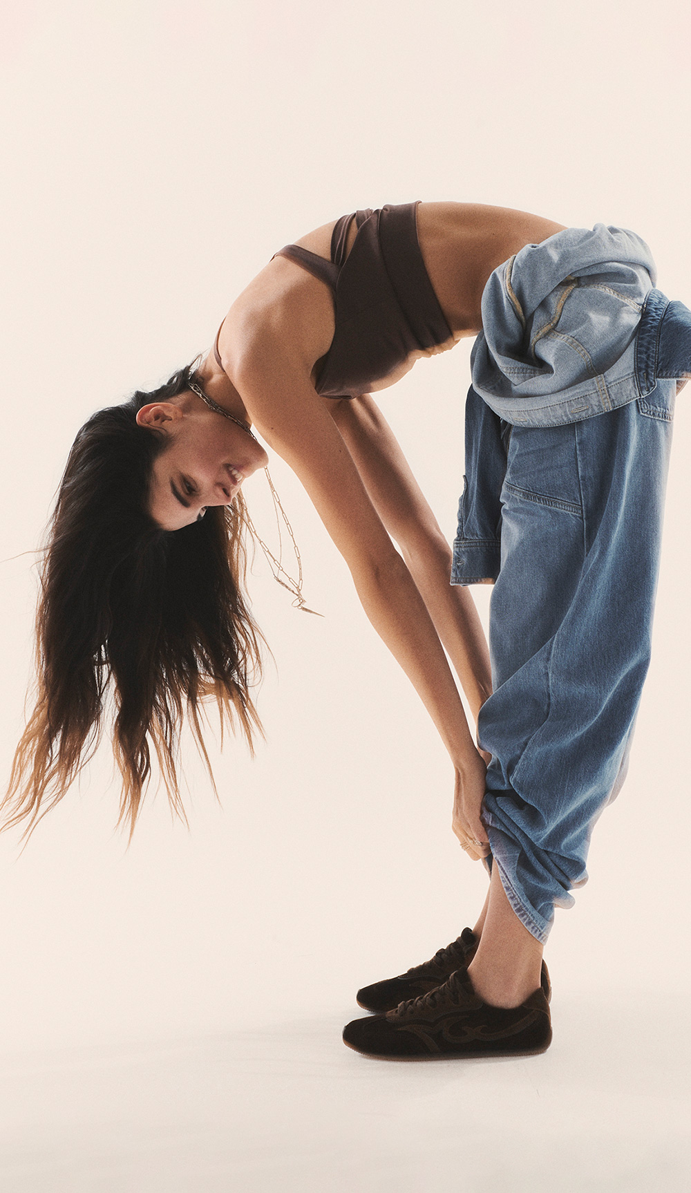 Brunette model wearing a blue jeans jumpsuits with brown bra
